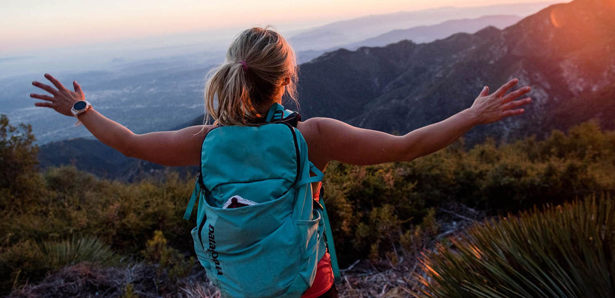 A woman standing at an overlook at sunset with her arms out wide