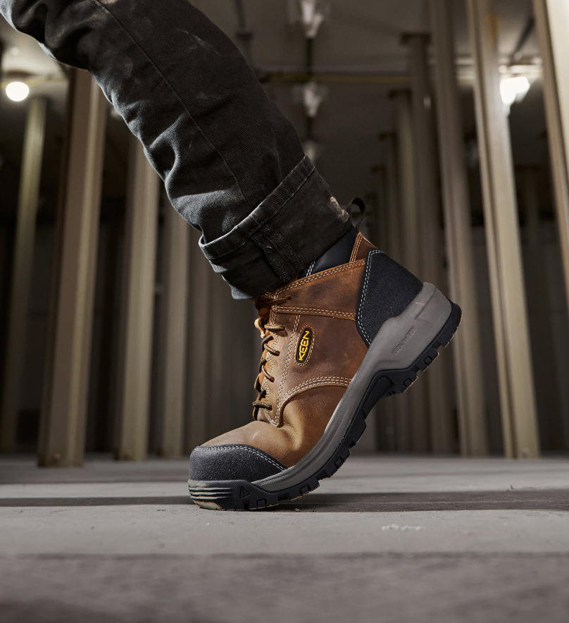 Knee-down shot of man wearing brown and  black Evanston work boot and walking down warehouse aisle. 